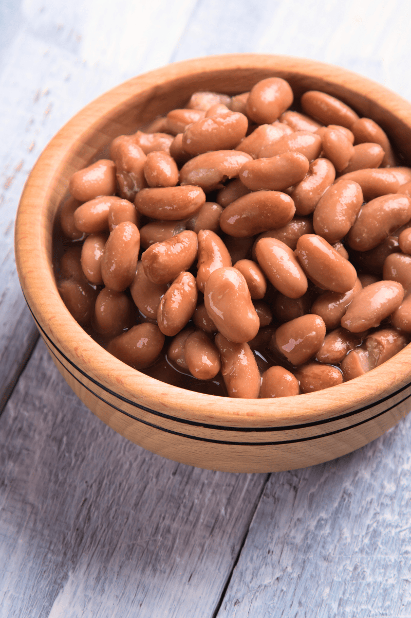 Close view of perfectly cooked beans in a wooden bowl on a light background.