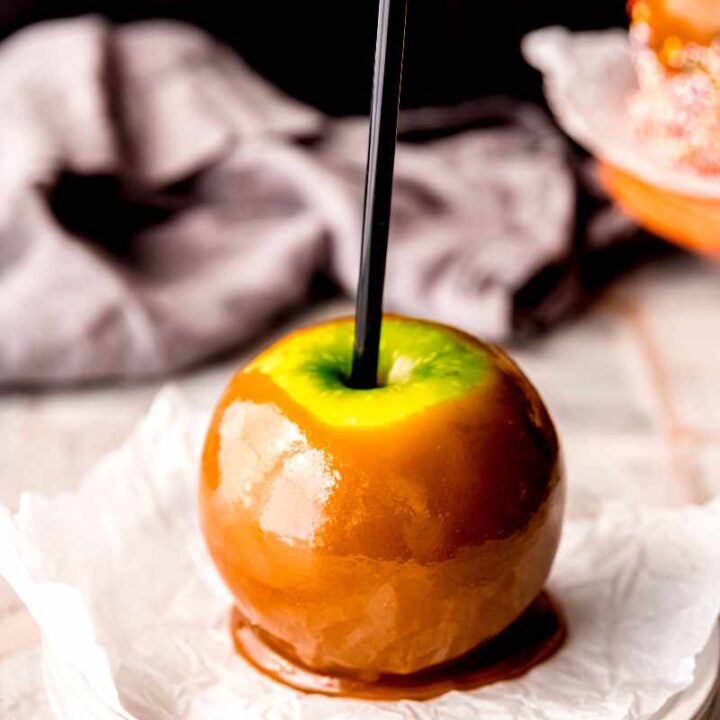 A caramel apple is served on a parchment paper lined plate.