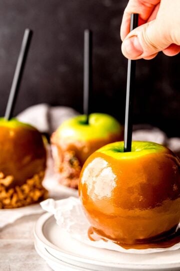 Hand reaches for a homemade caramel apple on a plate