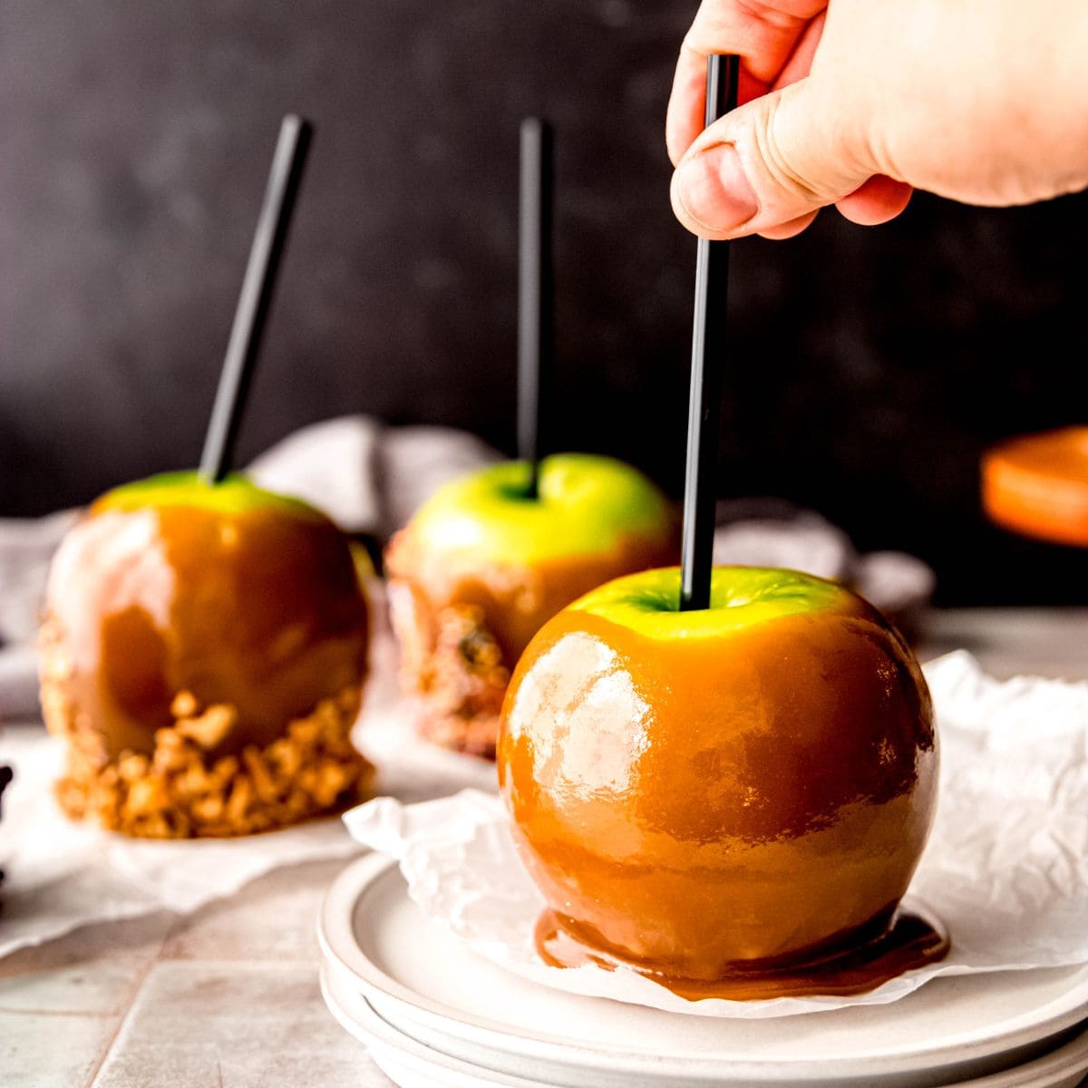 Hand reaches for a homemade caramel apple on a plate