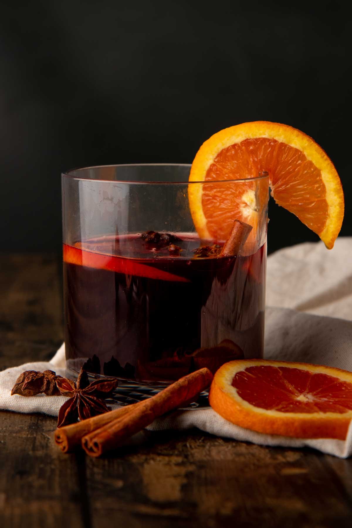 A glass of red wine apple cider sangria sits with an orange slice on the rim