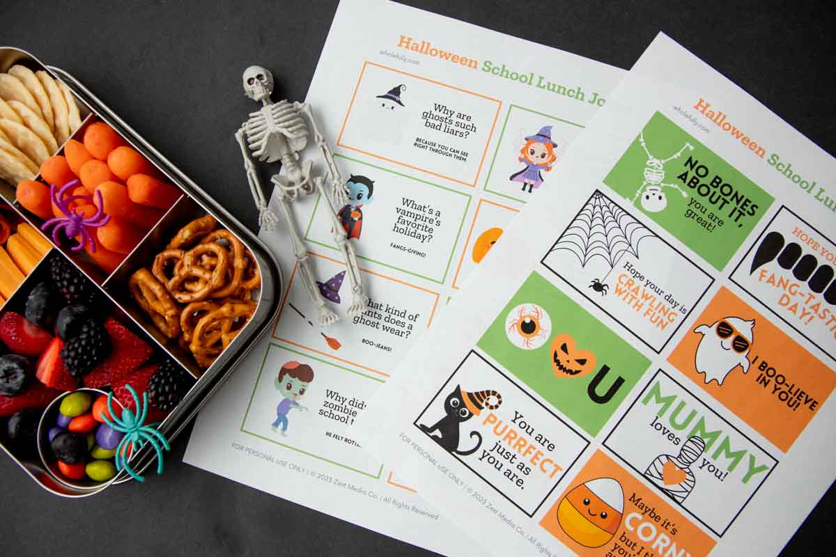 A plastic skeleton rests atop two sheets of printable Halloween notes beside a bento lunch.