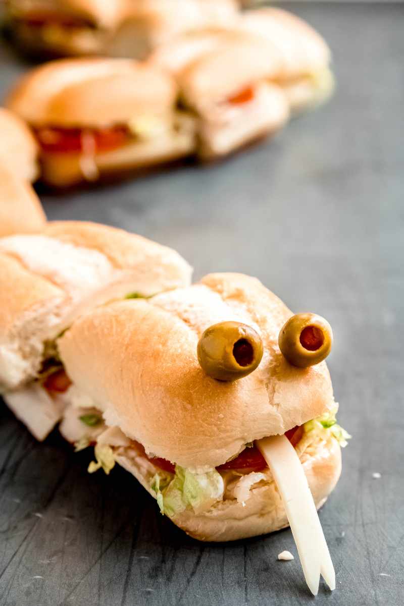 Close view of a Halloween party sub decorated to look like a snake with olive eyes and a forked cheese tongue.