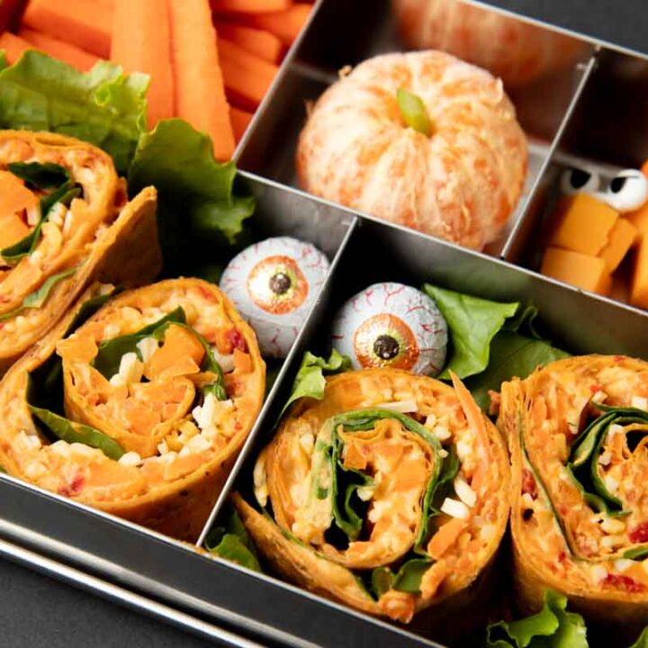 Halloween veggie pinwheels nestles into a bento-style lunchbox with other orange foods.