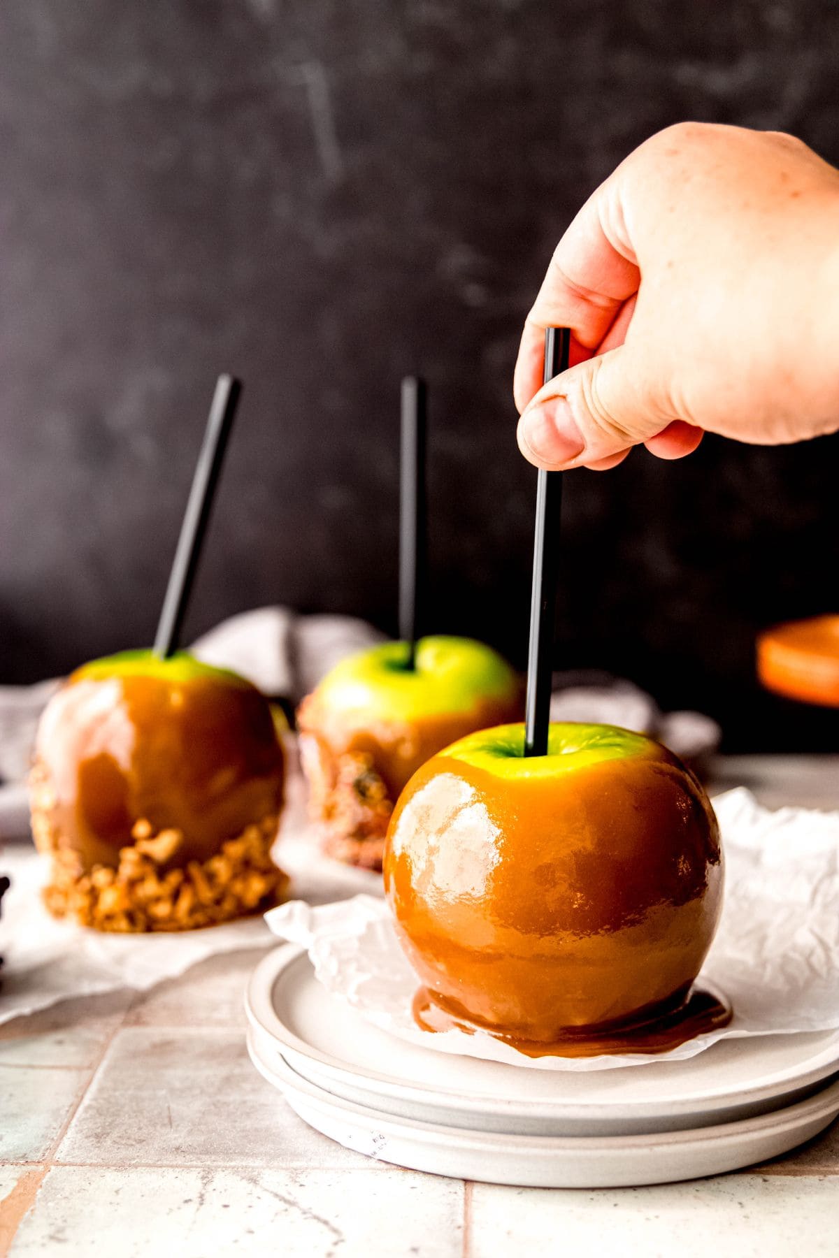 Hand reaches for a homemade caramel apple on a plate