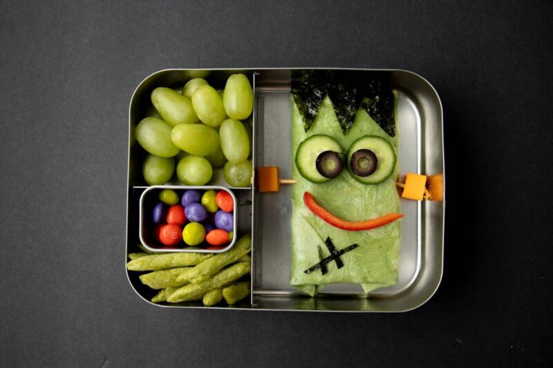 Halloween monster wrap lunch with green grapes and green snap pea snack crisps.