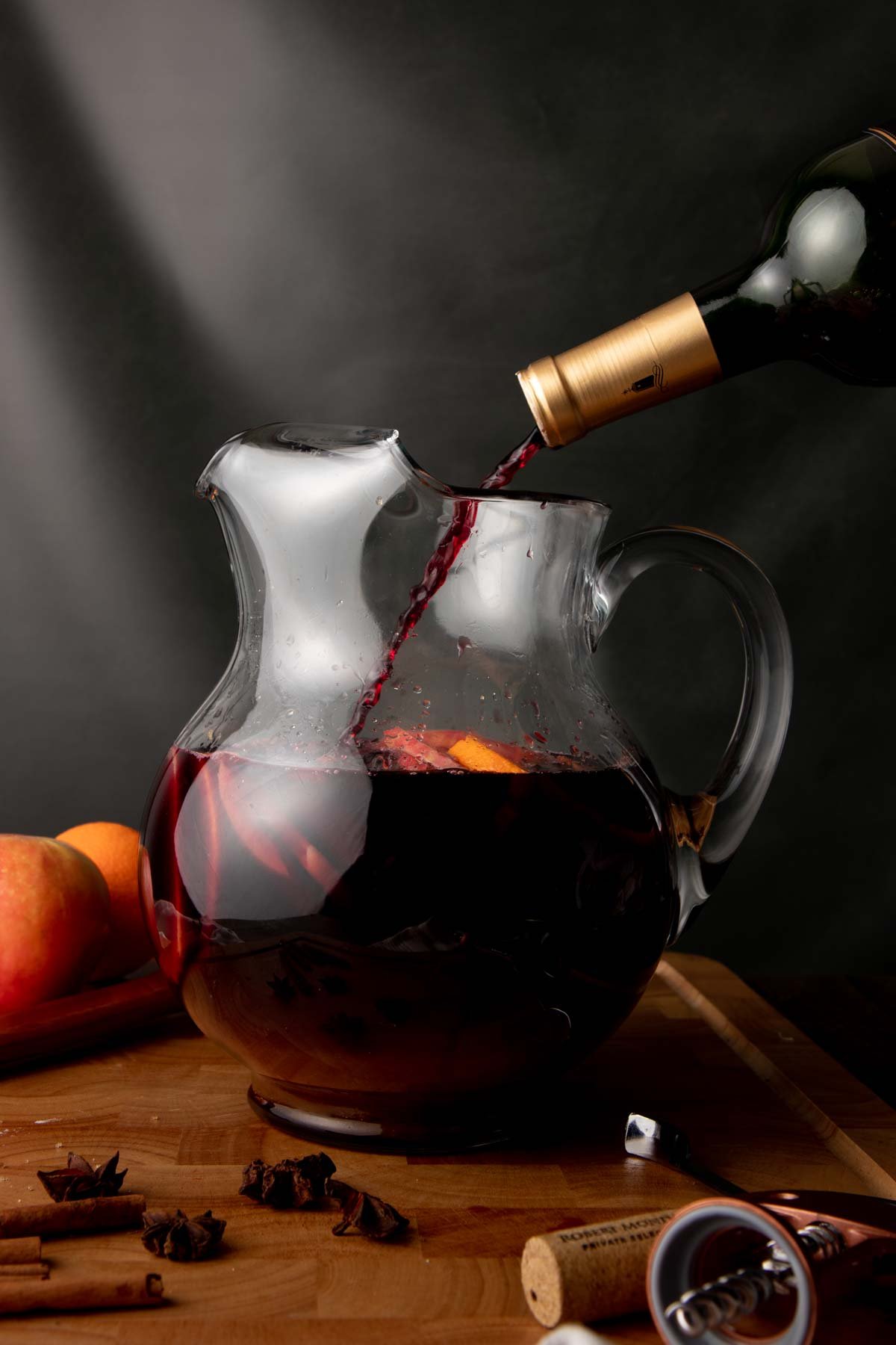 A bottle of red wine is poured into a glass pitch of sangria