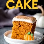 A piece of pumpkin cake with cream cheese frosting on a white dish with an edible pumpkin garnish. A text overlay reads, "Pumpkin Cake."