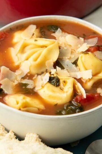 A bowl of tortellini soup garnished with shaved parmesan