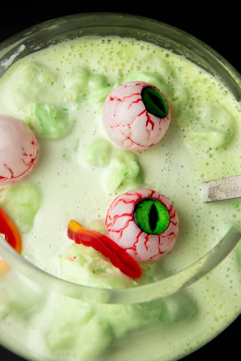 Top view of spooky plastic bloodshot eyes and gummy works floating on top of a serving bowl of a festive Halloween drink for kids.
