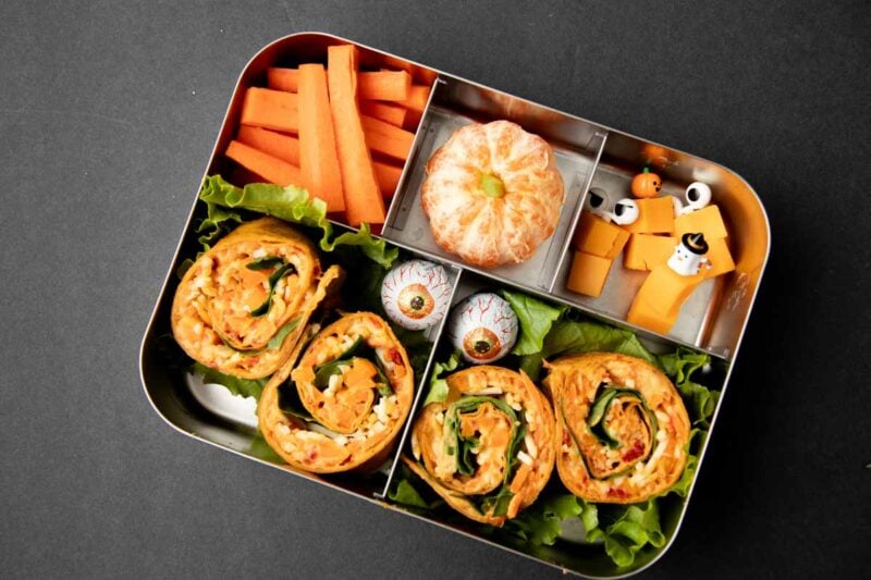 Overhead of a spooky pinwheel bento with candy eyes and orange foods.