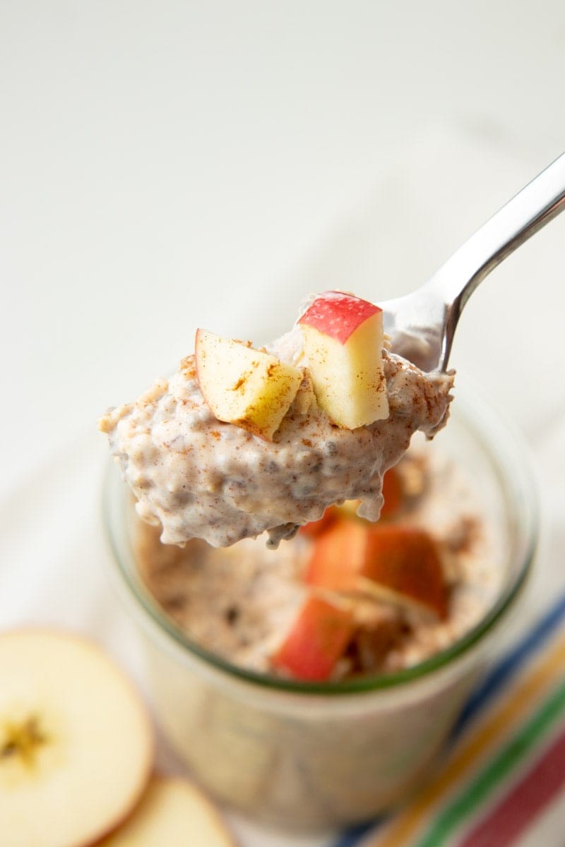 Close view of a spoonful of creamy overnight oats topped with chopped fruit and cinnamon.