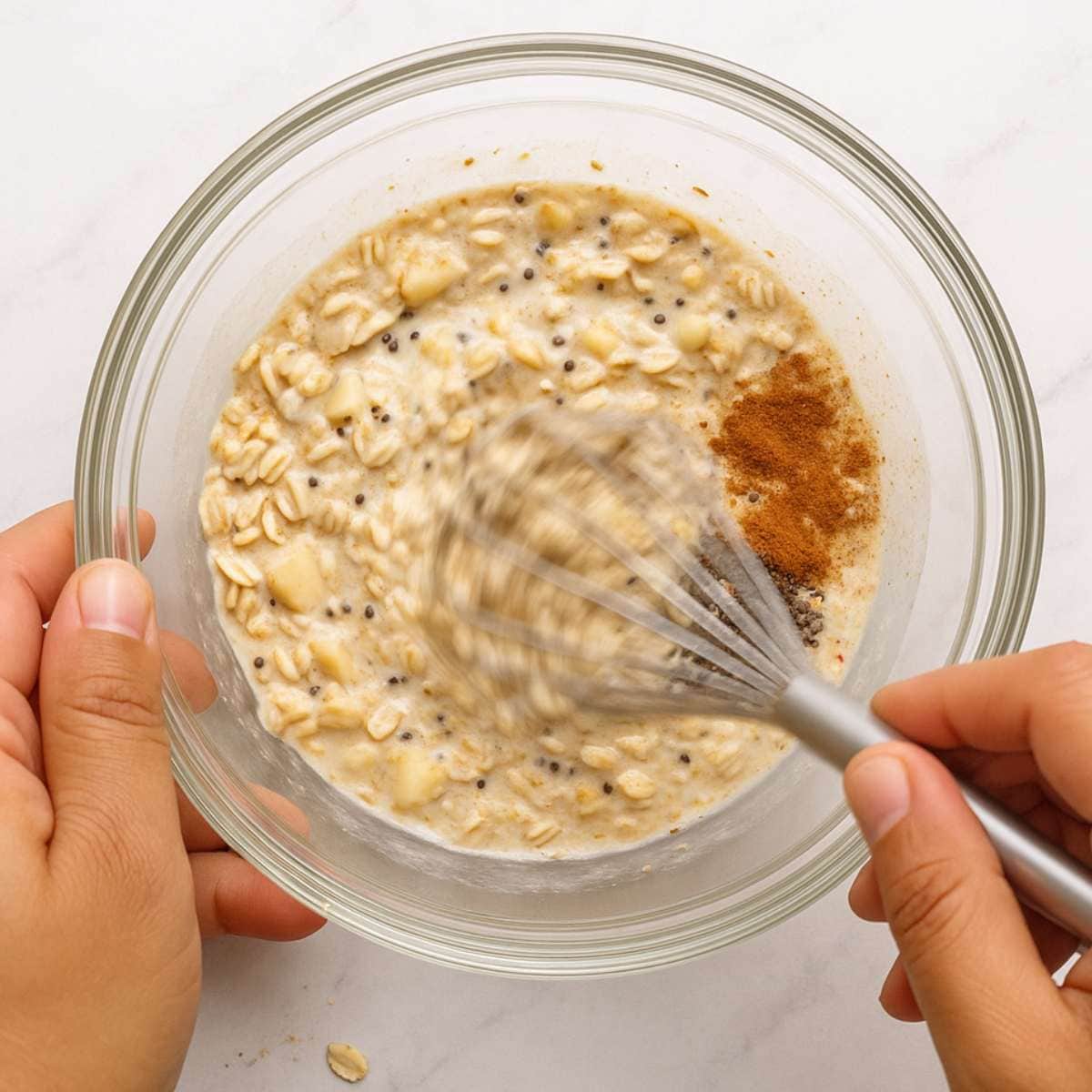 Hands whisk together apple cinnamon overnight oats in a glass bowl