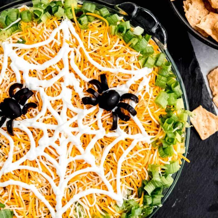 Halloween taco dip served on a black slate board with a bowl of tortilla strips nearby.