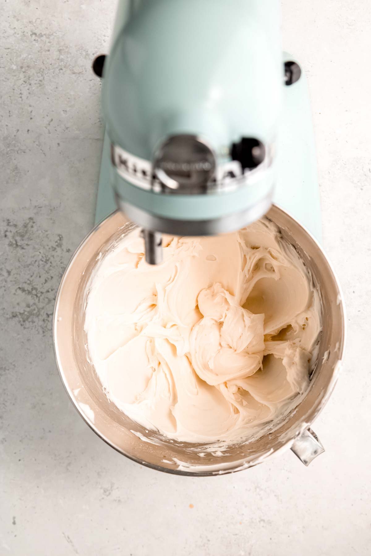 A blue stand mixer whipping fluffy cream cheese frosting