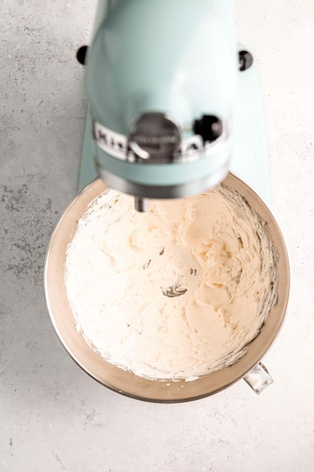 A blue stand mixer blending together ingredients for cream cheese frosting