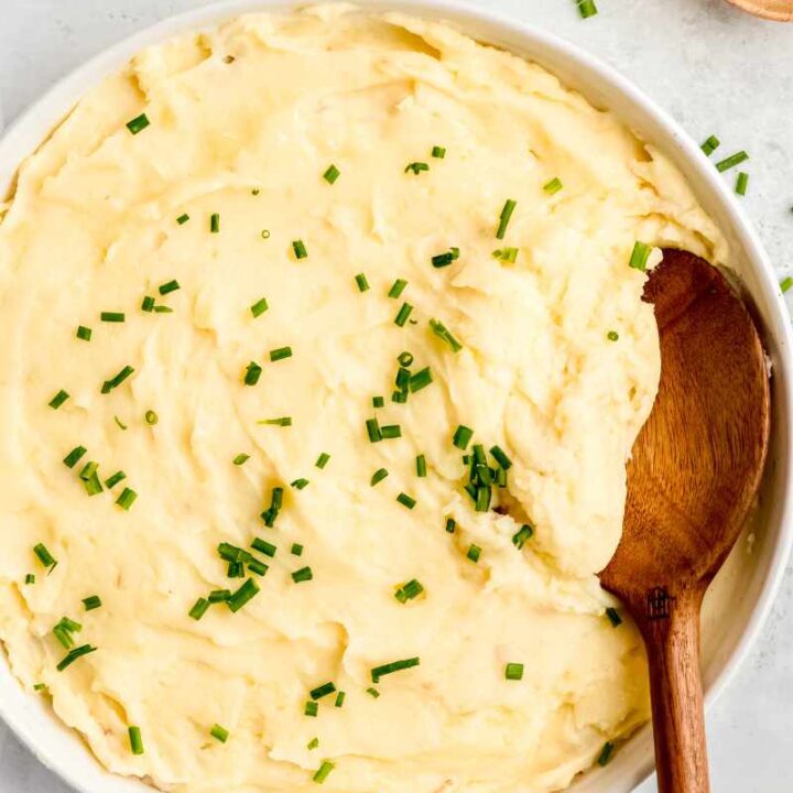 A spoon dips into a creamy potato side dish served family-style in a large white bowl.
