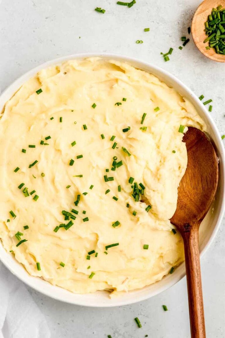 A spoon dips into a creamy potato side dish served family-style in a large white bowl.