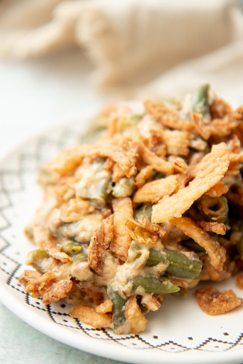 Close view of a serving of green bean casserole on plate topped with crispy fried onions.