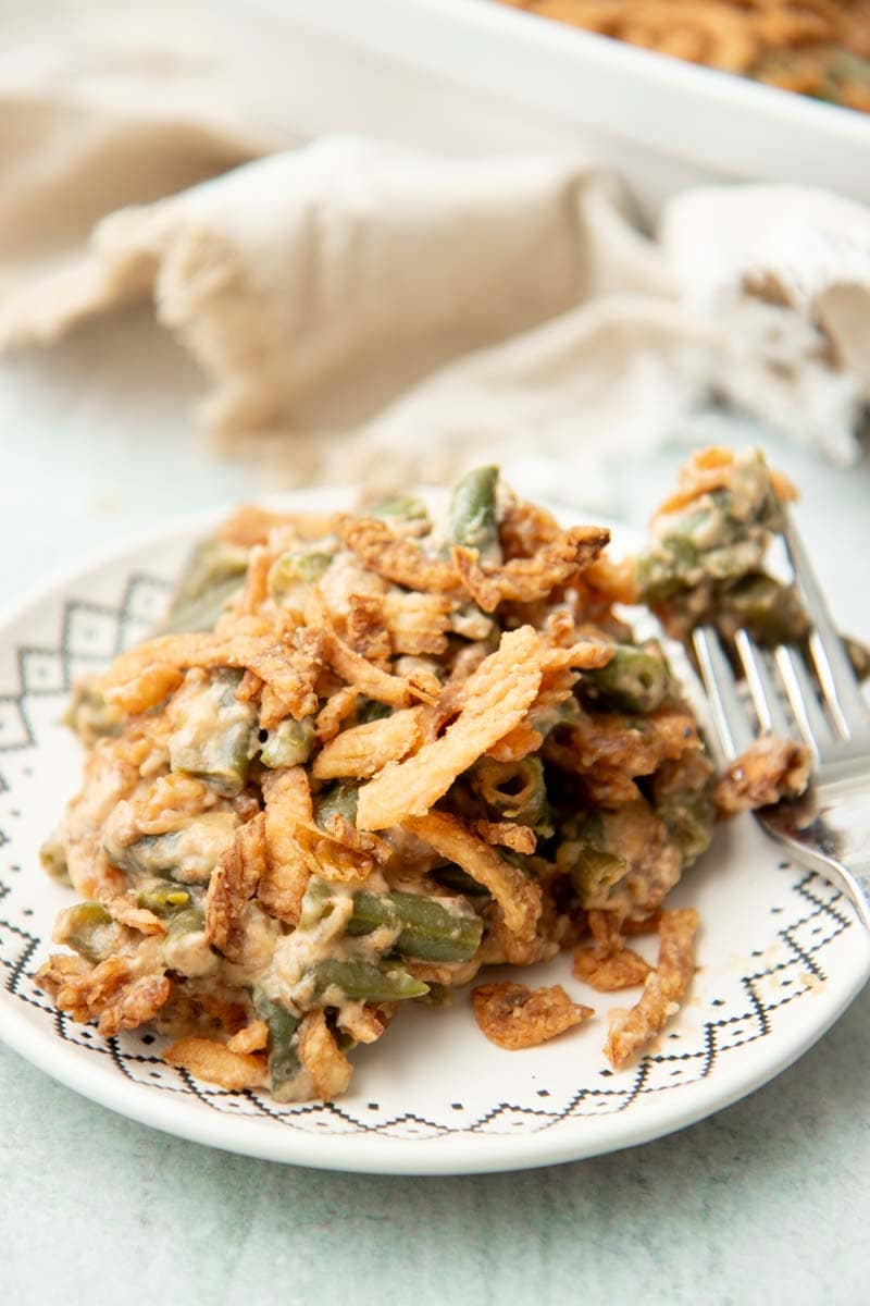 A generous helping of green bean casserole garnished with crispy fried onions rests on a white plate with decorative black trim.