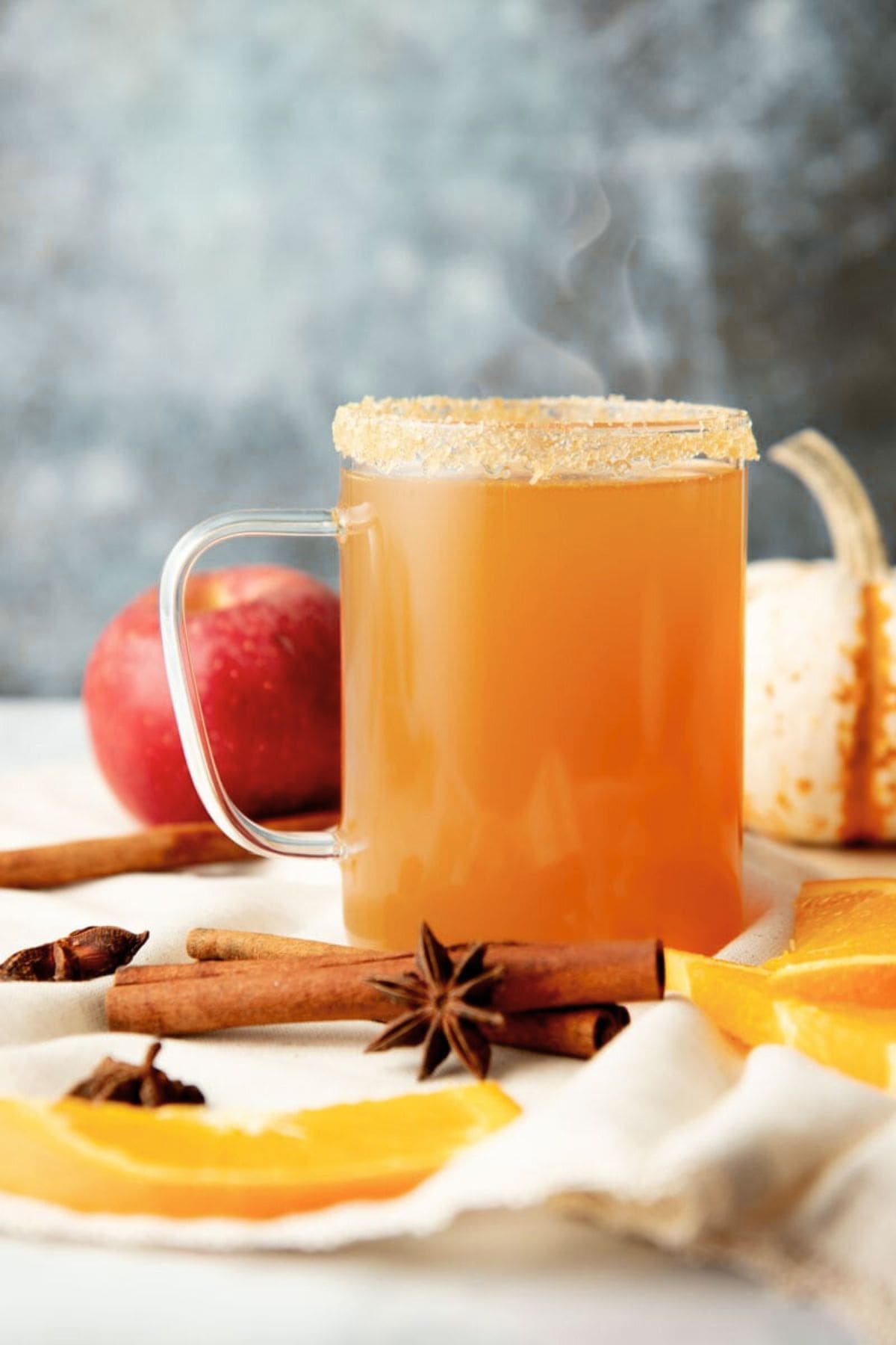 Steam rises out of a clear glass mug of spiked apple cider