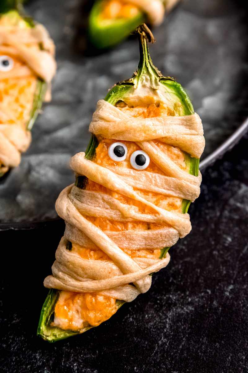 Close view of a mummy jalapeno popper standing up against the edge of a serving platter.
