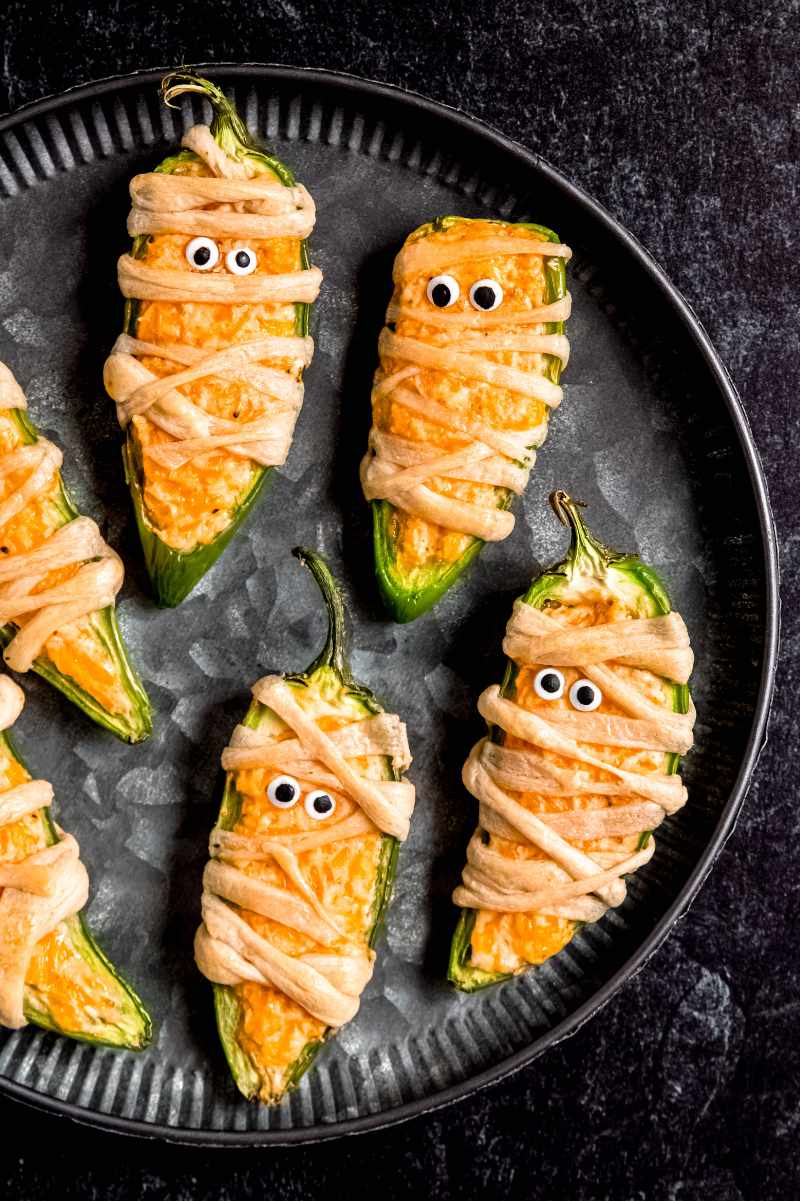 Overhead of a dark serving platter filled with mummy jalapeno poppers.