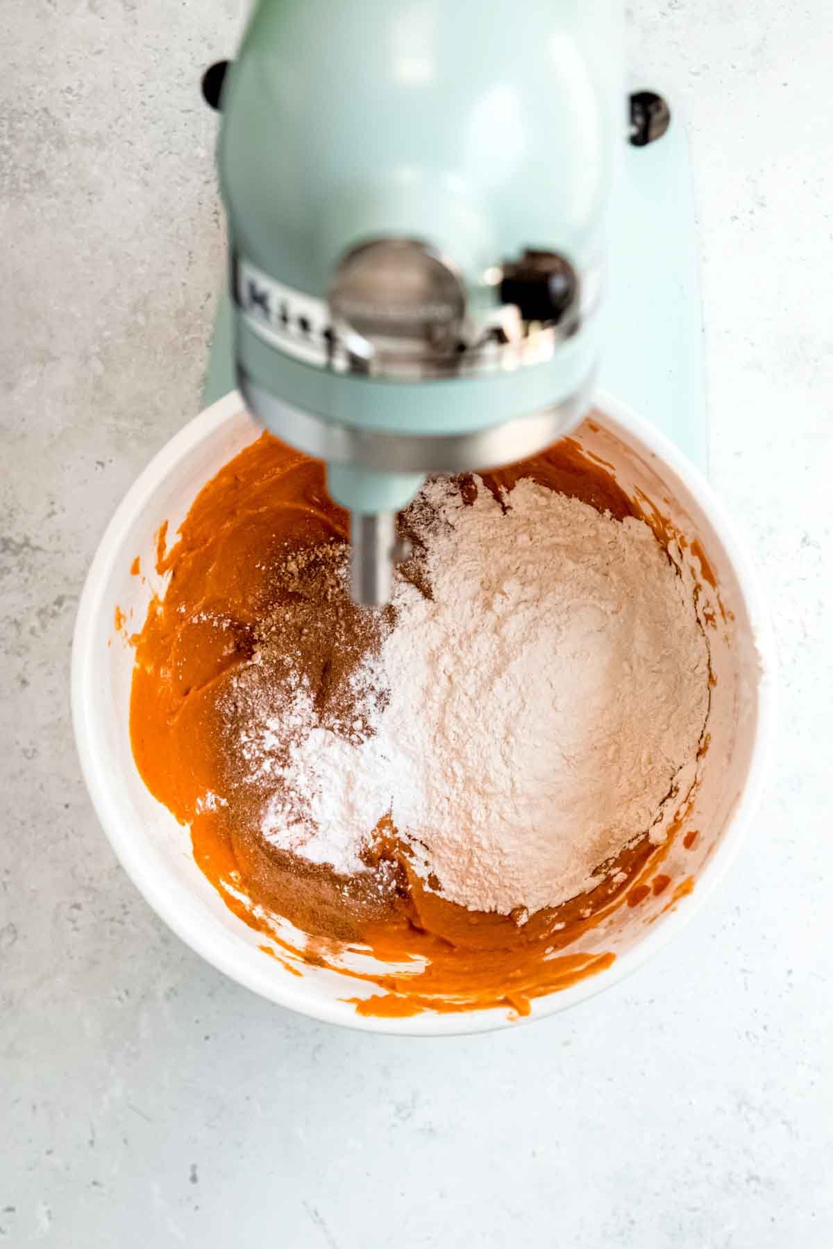 A blue stand mixer blends together wet and dry ingredients for pumpkin cake