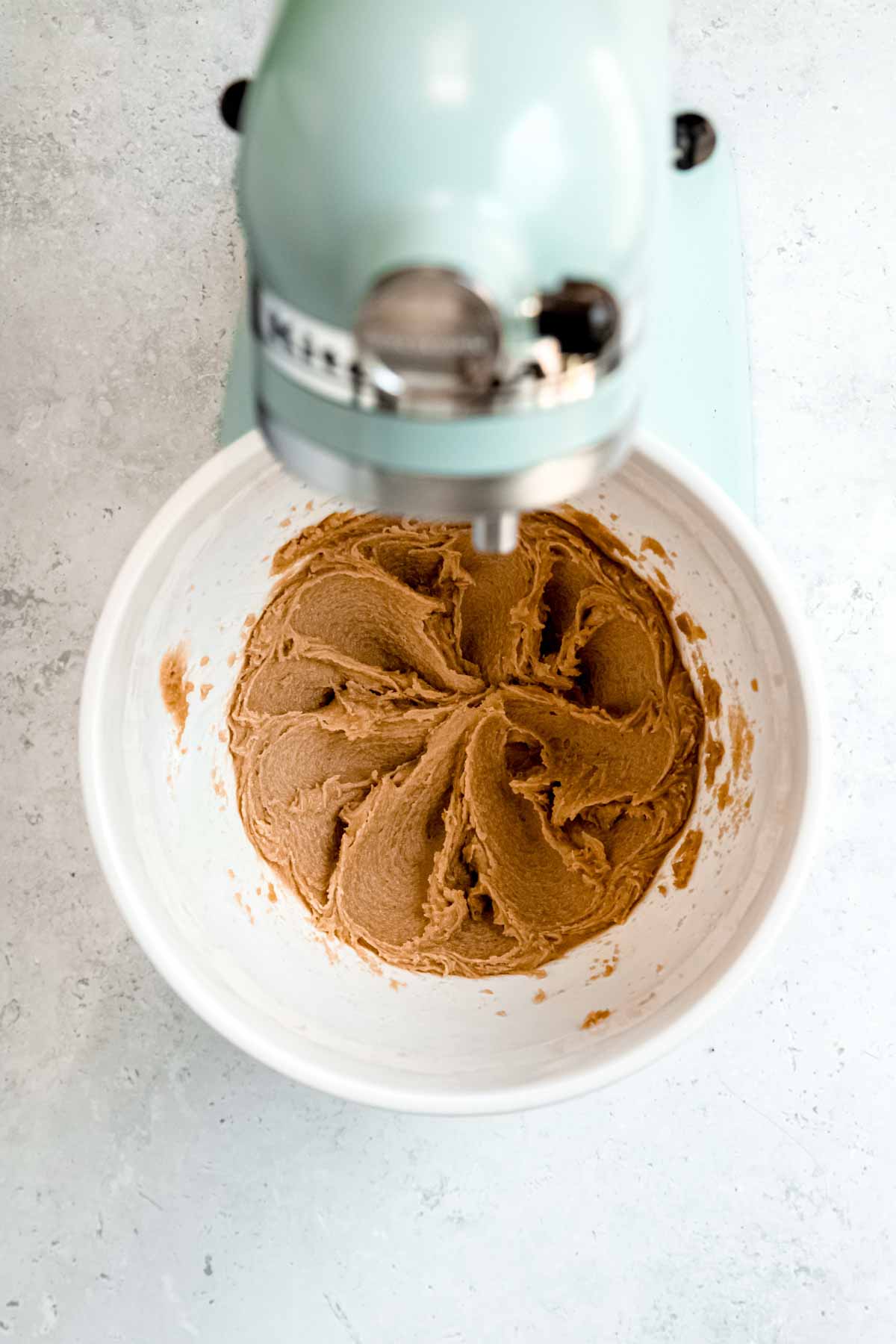A blue stand mixer blends together butter and brown sugar in a white bowl