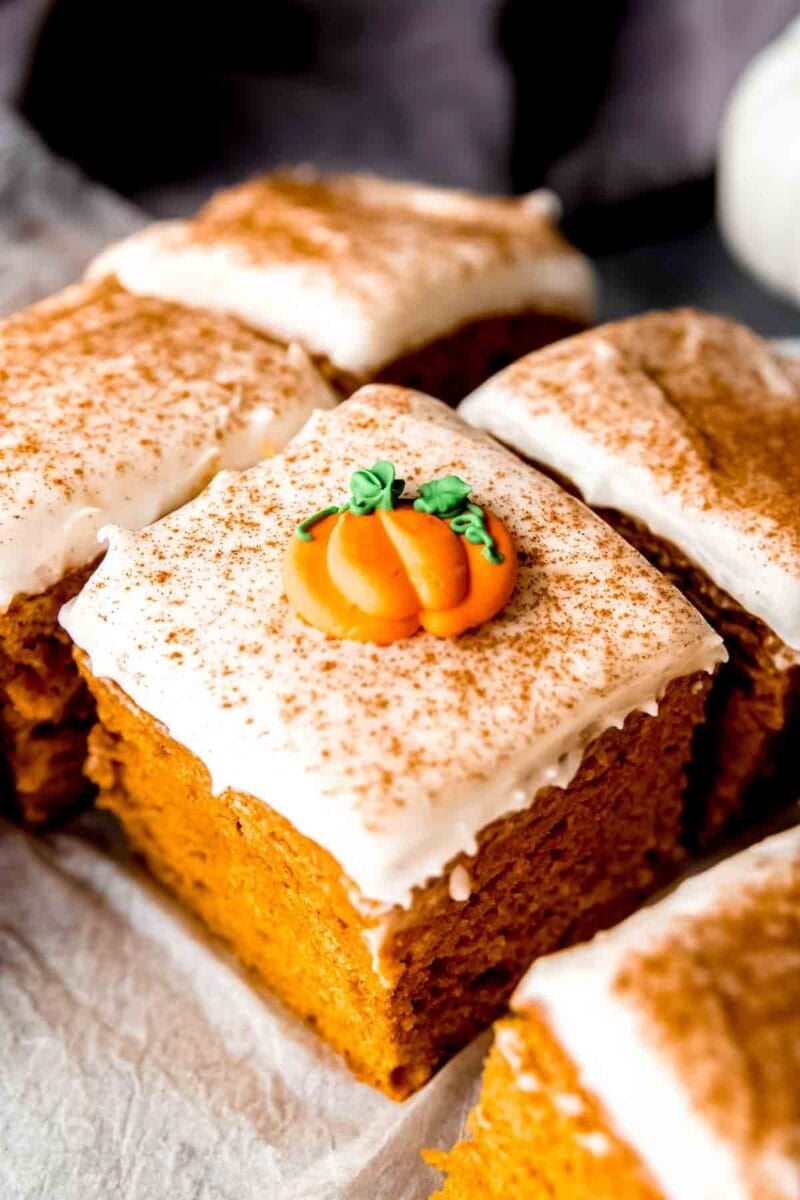 Slices of pumpkin cake with cream cheese frosting with pumpkin sugar garnishes sit on top of a serving platter.