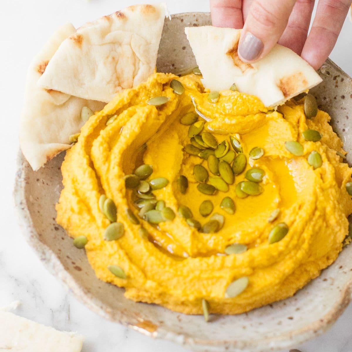 Scooping pumpkin hummus out of a bowl with a pita wedge