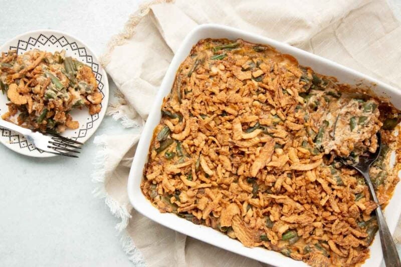 Overhead of a baking dish filled with green bean casserole, a serving scooped onto a plate beside it.