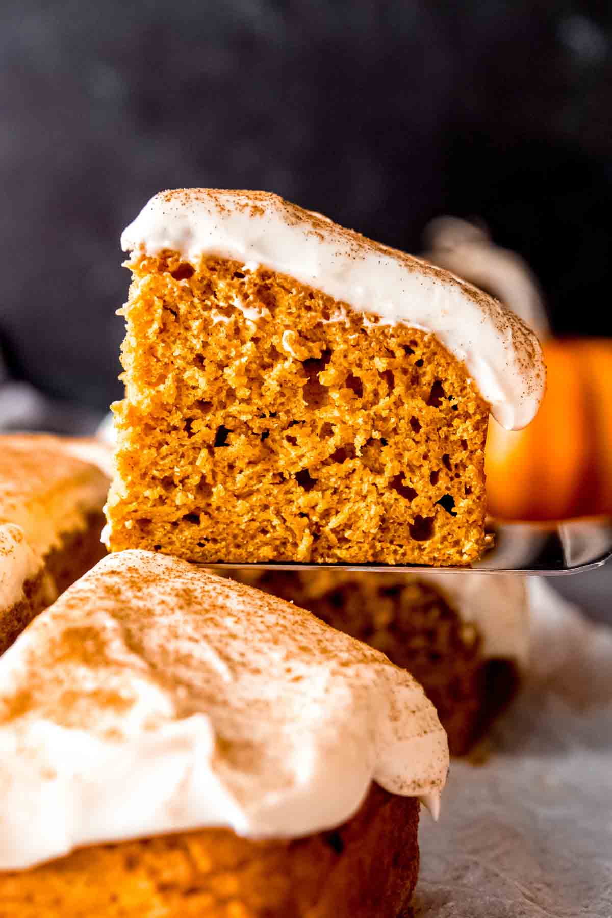 A slice of pumpkin cake with cream cheese frosting on a cake server