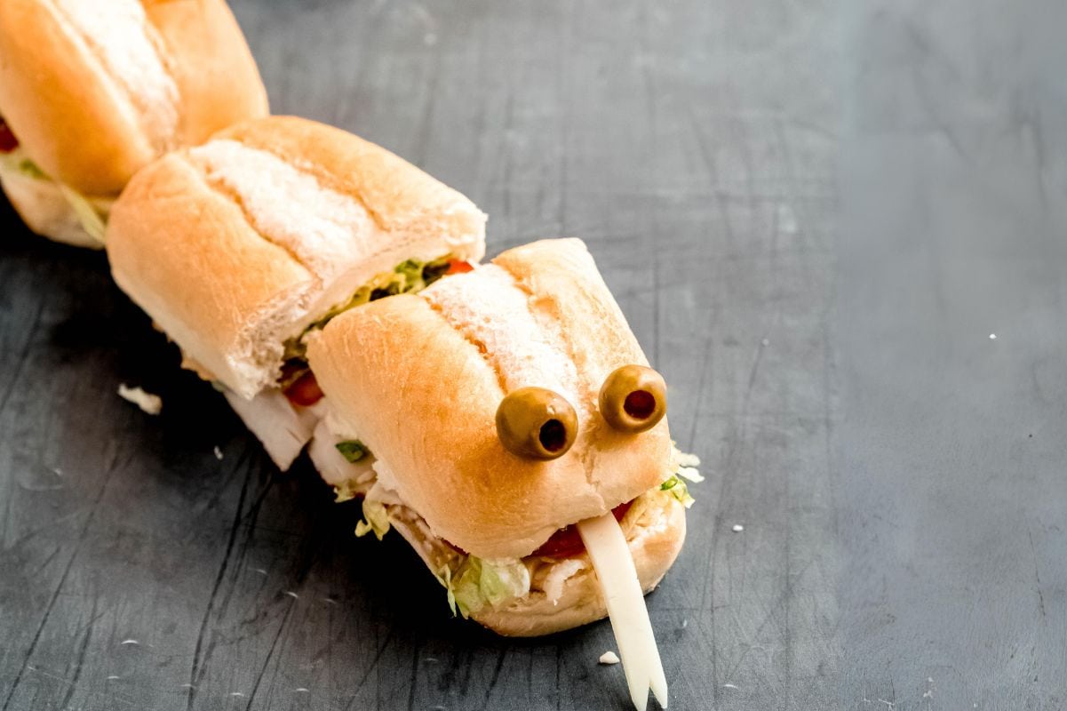 A snakewich party sub made from turkey and cheese cut into segments and garnished with olive eyes and a forked tongue of cheese.