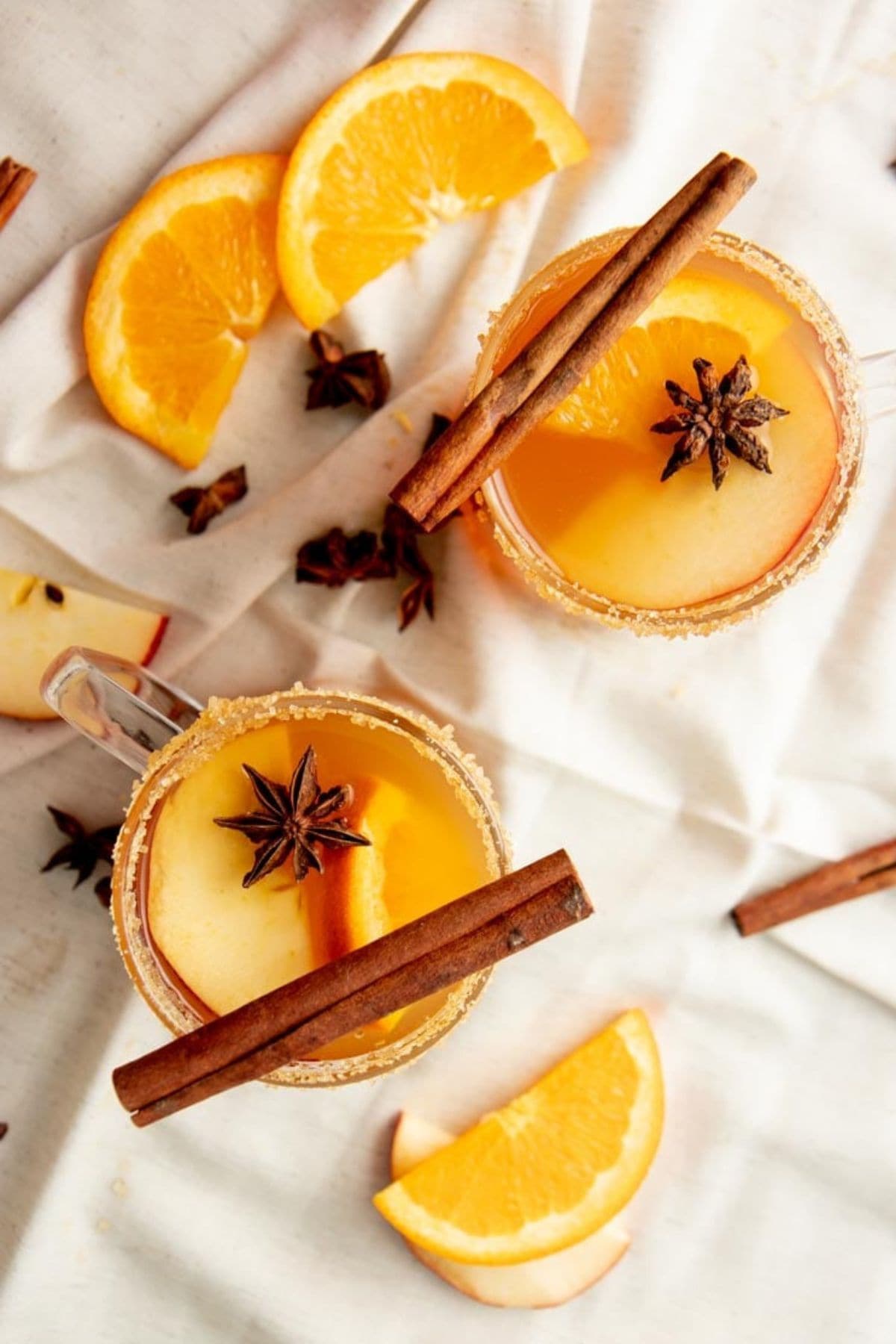 Two mugs of spiked apple cider sit on a white kitchen towel