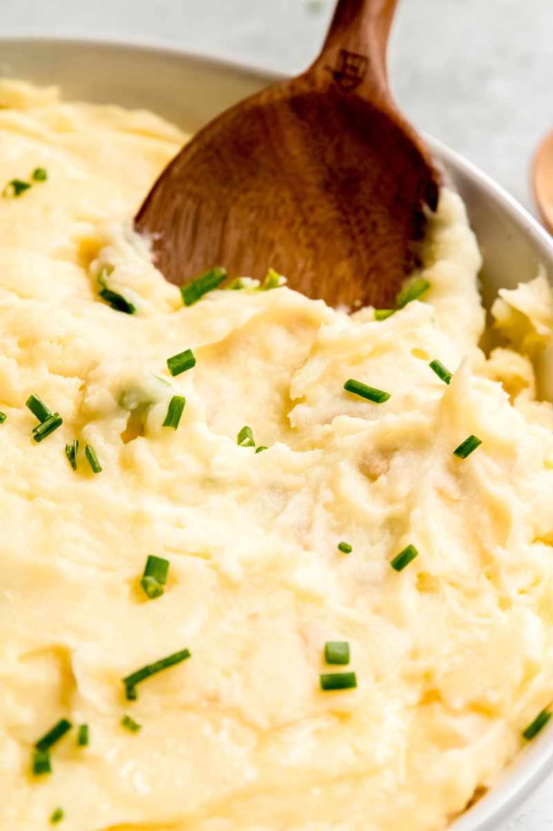 A wooden spoon dips into creamy potatoes in a wide bowl.