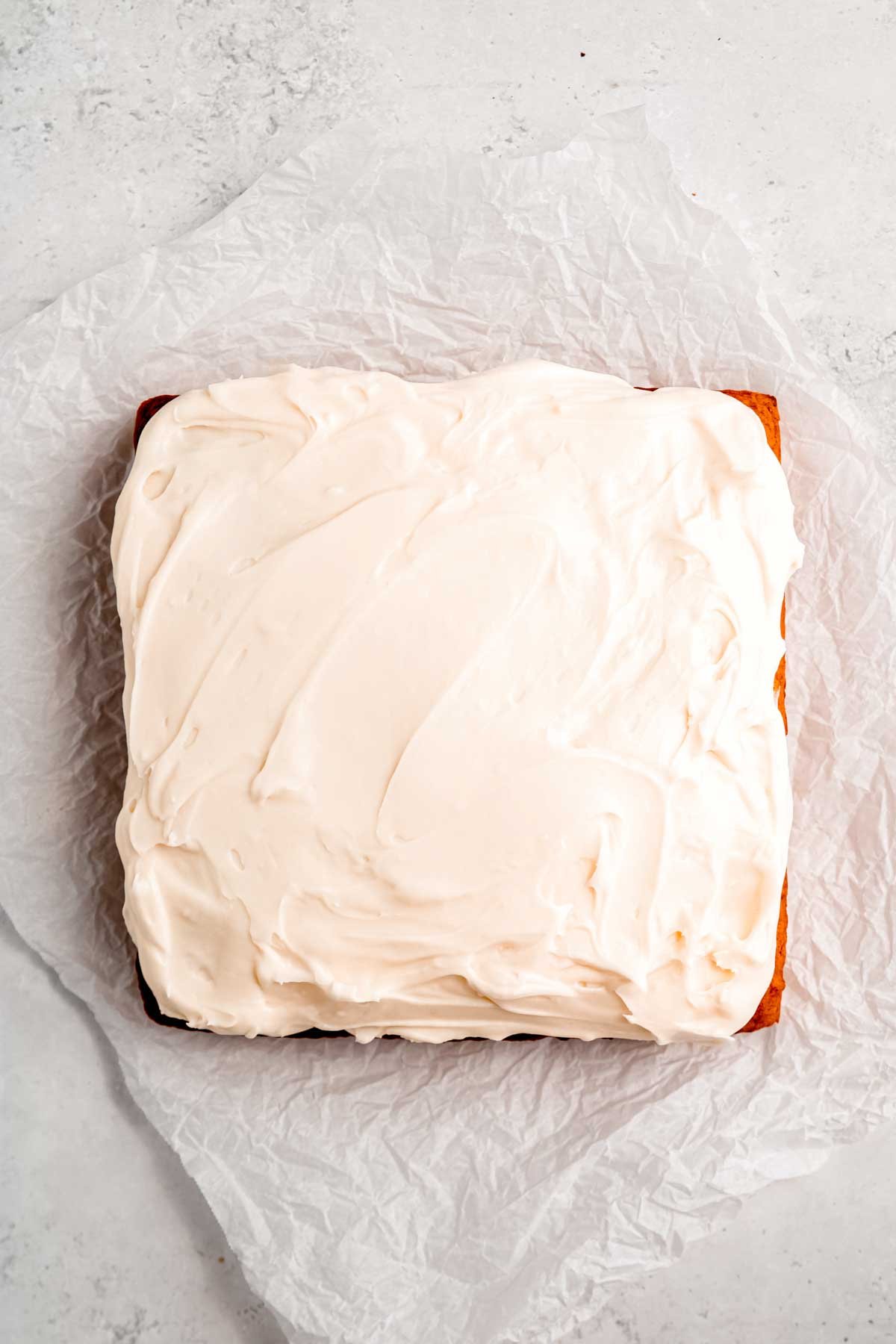 An uncut pumpkin cake frosted with cream cheese frosting on a white countertop