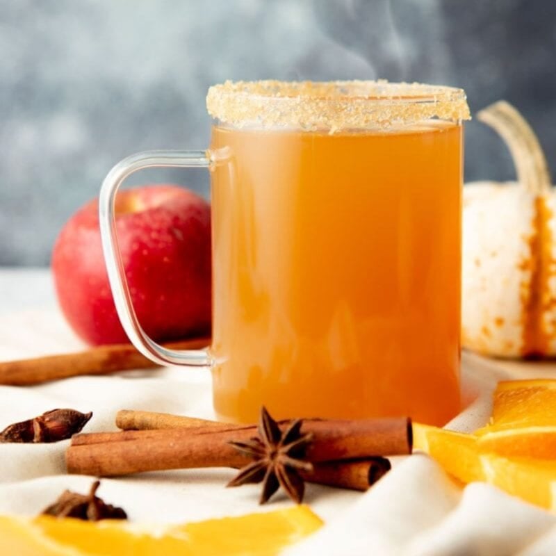 Steam rises out of a clear glass mug of spiked apple cider
