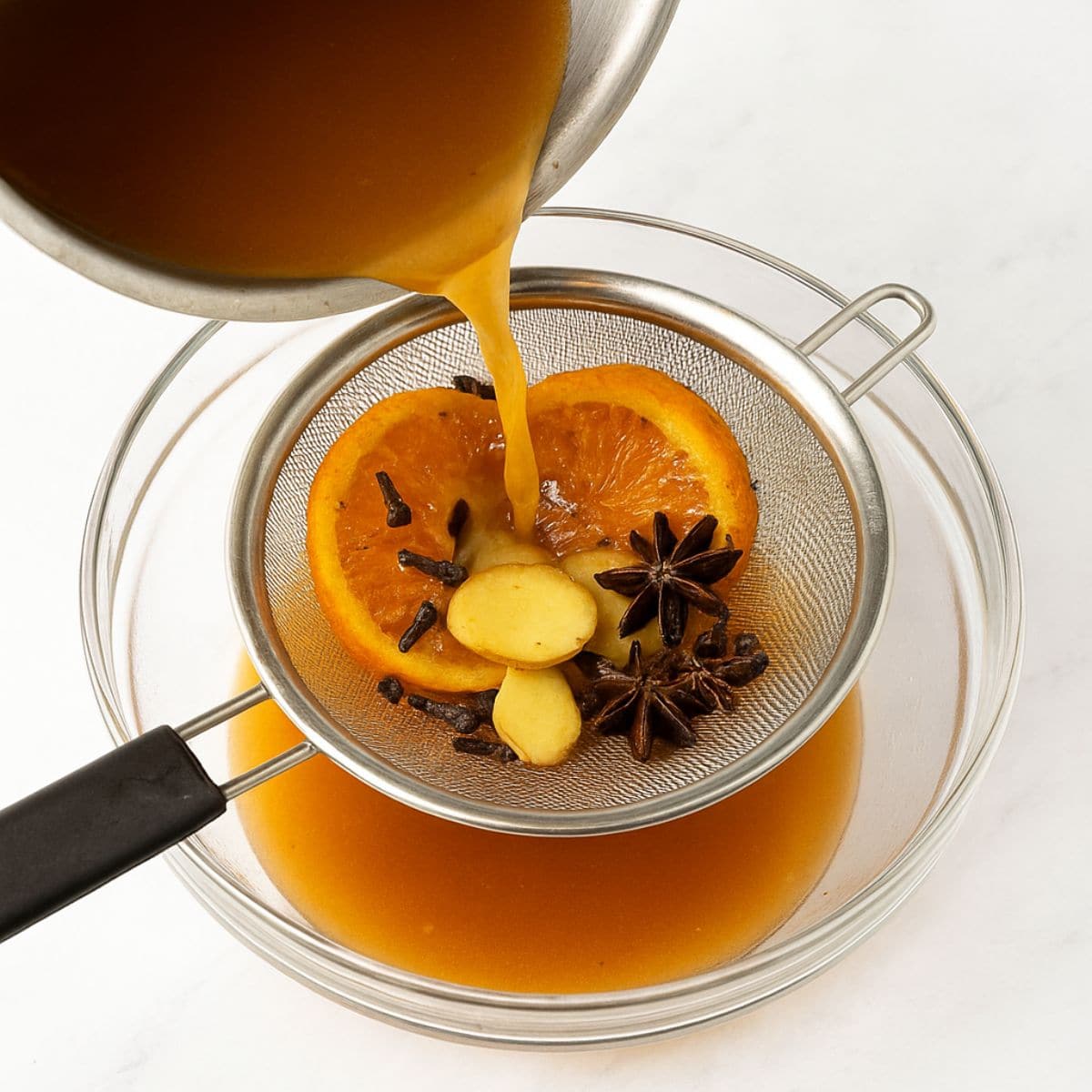 Straining whole spices out of hot apple cider using a metal sieve