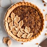 Top view of a whole vegan chocolate pie with walnuts in a white pie plate on a light counter.
