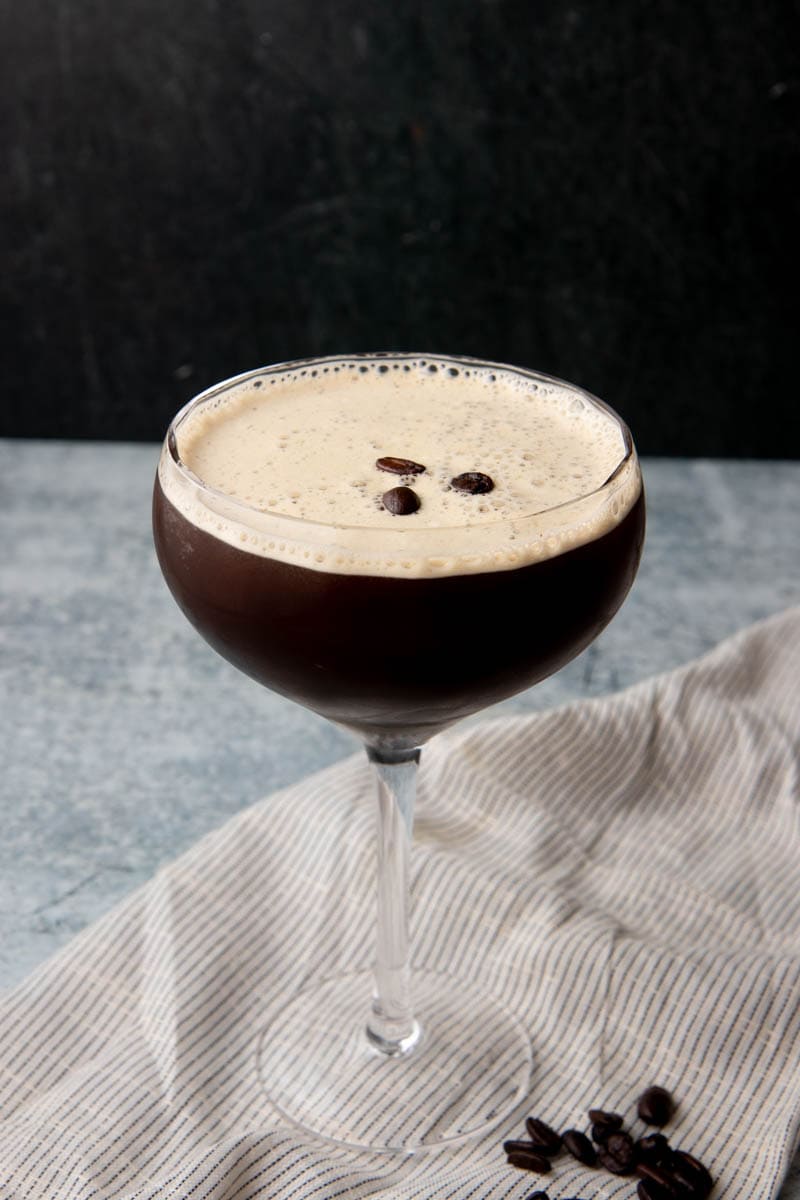 A coffee cocktail served in a coupe glass on a grey counter with a dark background.