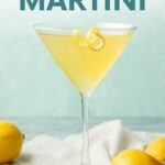 Front view of a limoncello martini with a lemon twist on the rim, whole lemons near the foot of the glass. A text overlay reads, "Limoncello Martini."