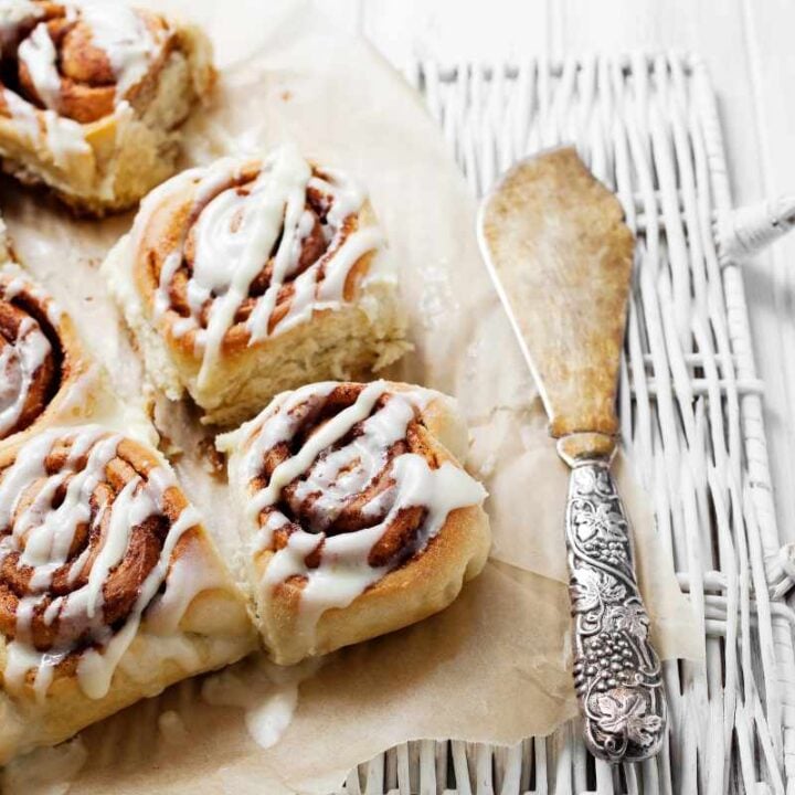 A white wicker serving tray with frosted morning buns on parchment paper and a decorative serving knife.