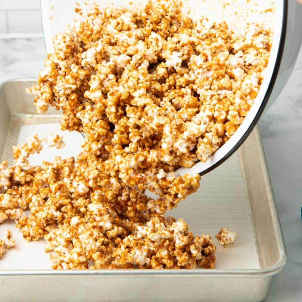 Pouring caramel corn from a bowl onto a parchment covered baking sheet to cool