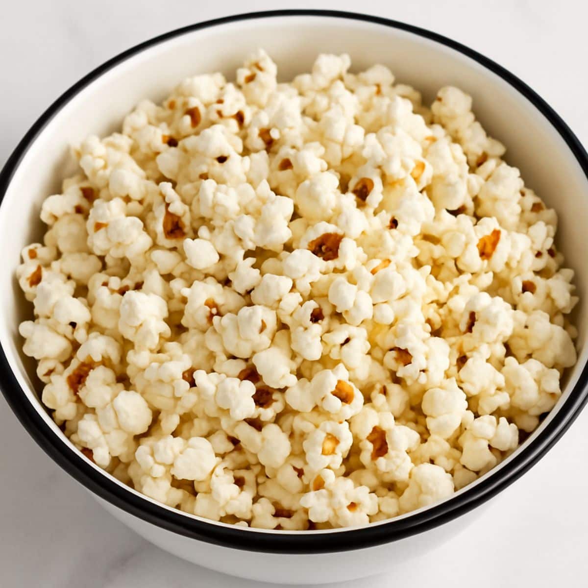 Popped popcorn in a white and black bowl on a white countertop