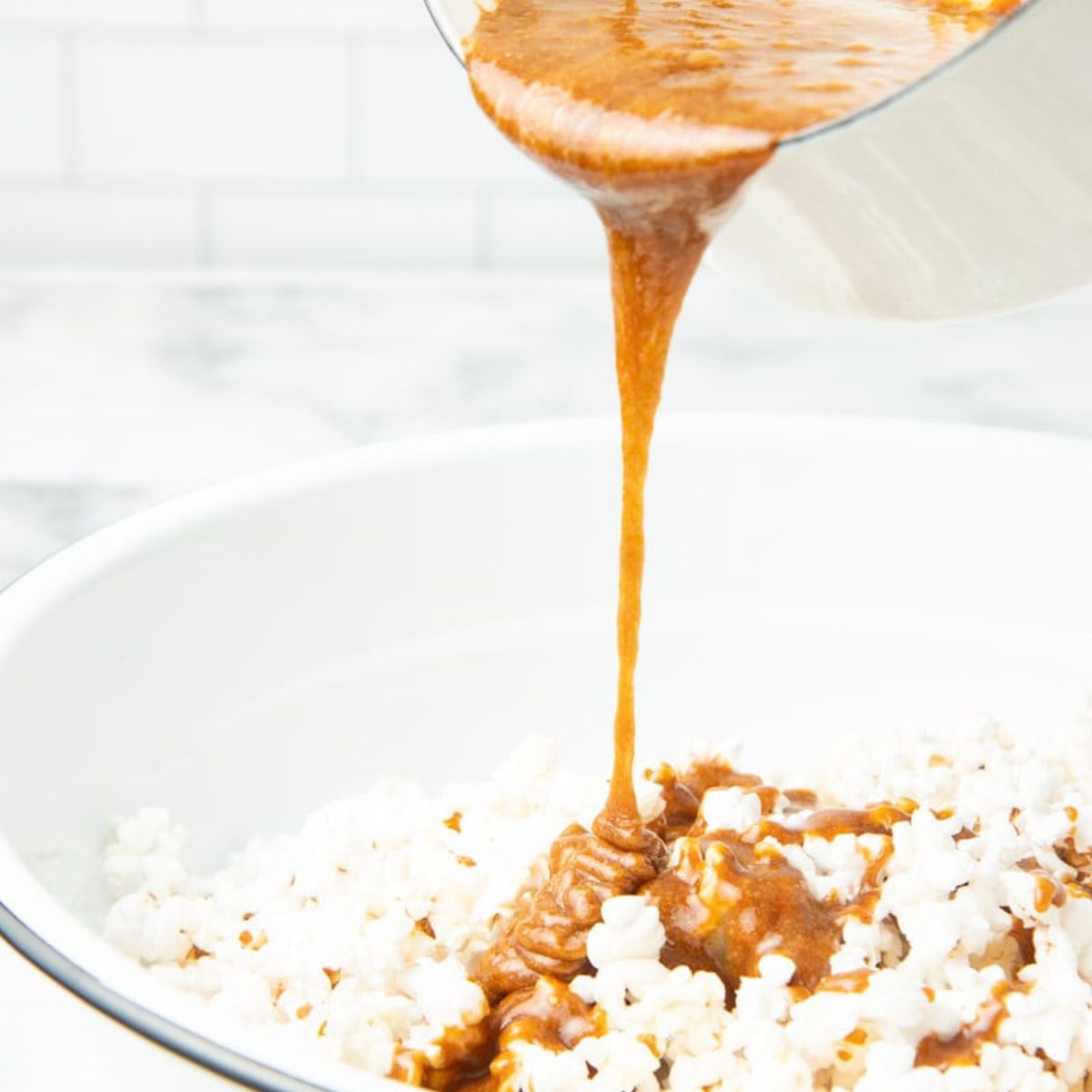 Pouring caramel onto popcorn in a white mixing bowl