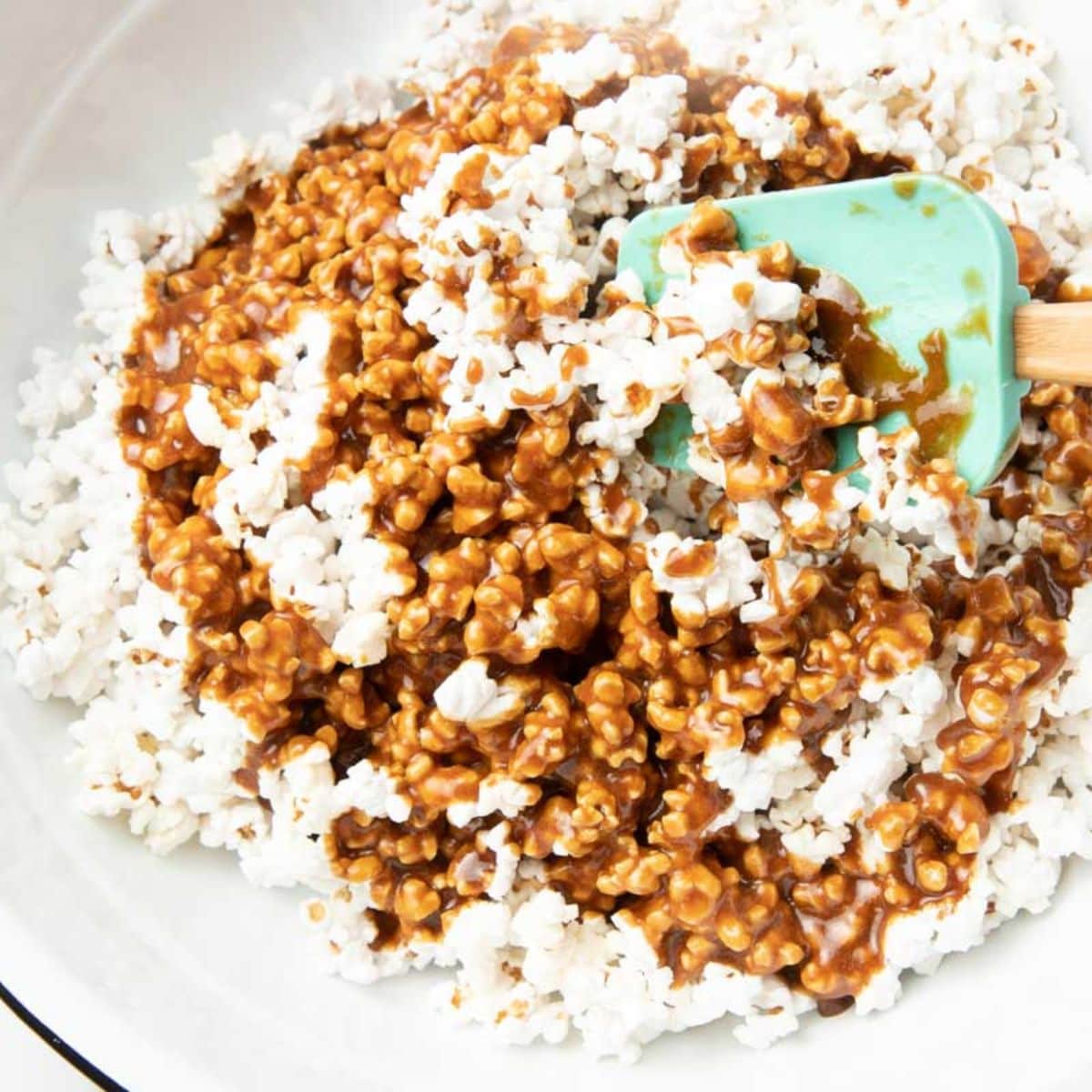 Stirring caramel popcorn in a large white bowl