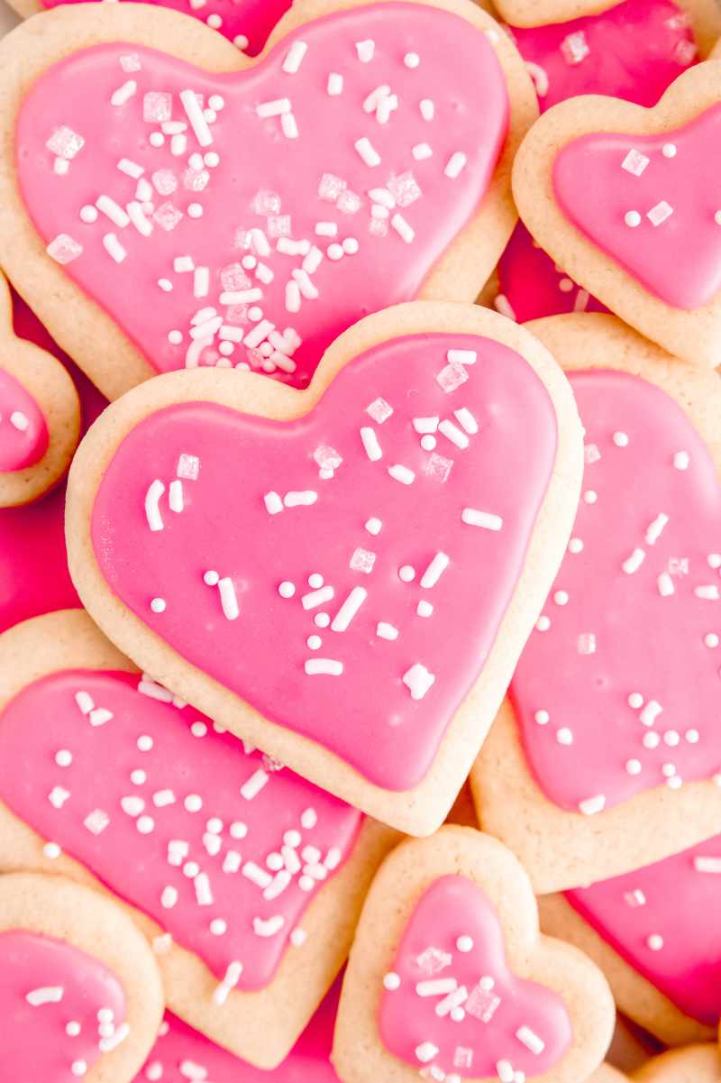 Close view of sugar cookie hearts piled high with pink frosting and white sprinkles.