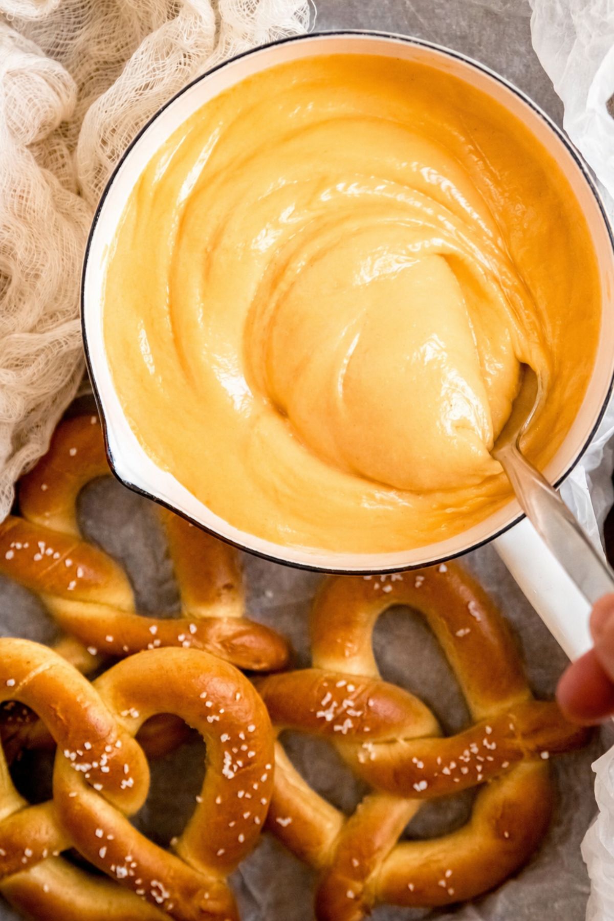 A pot of creamy beer cheese dip with a spoon resting inside, surrounded by warm salted soft pretzels.