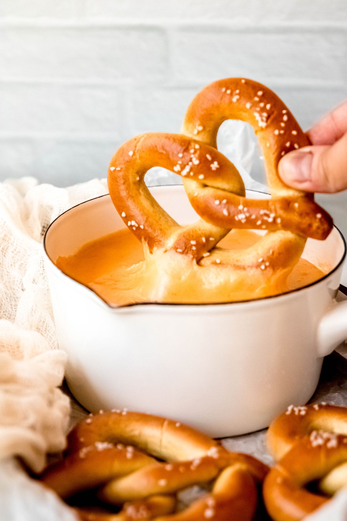 A salted soft pretzel dipped into a pot of warm beer cheese, with melted cheese stretching between the pretzel and the pot.